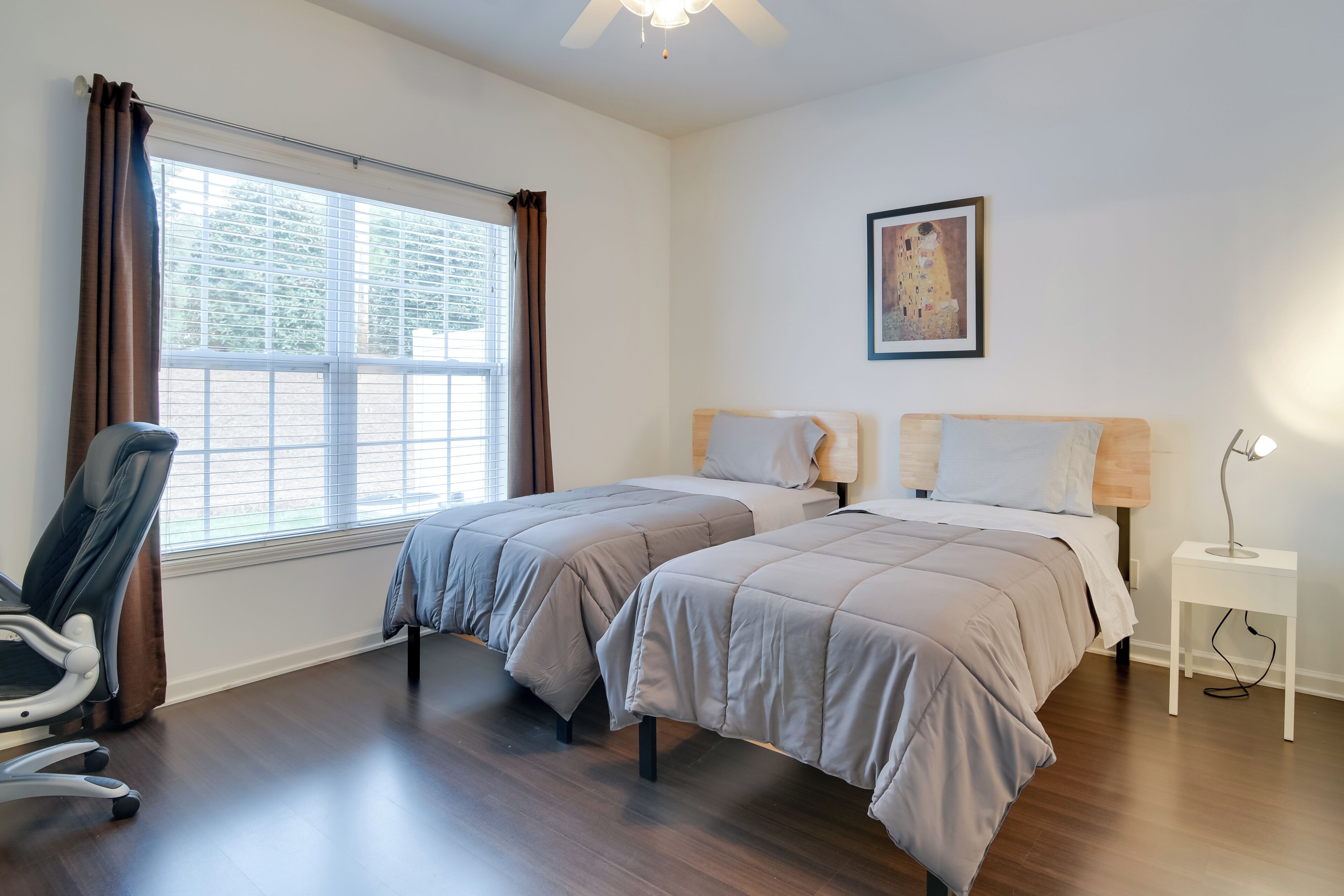 A bedroom with two beds, a chair, a nightstand, and a ceiling fan.