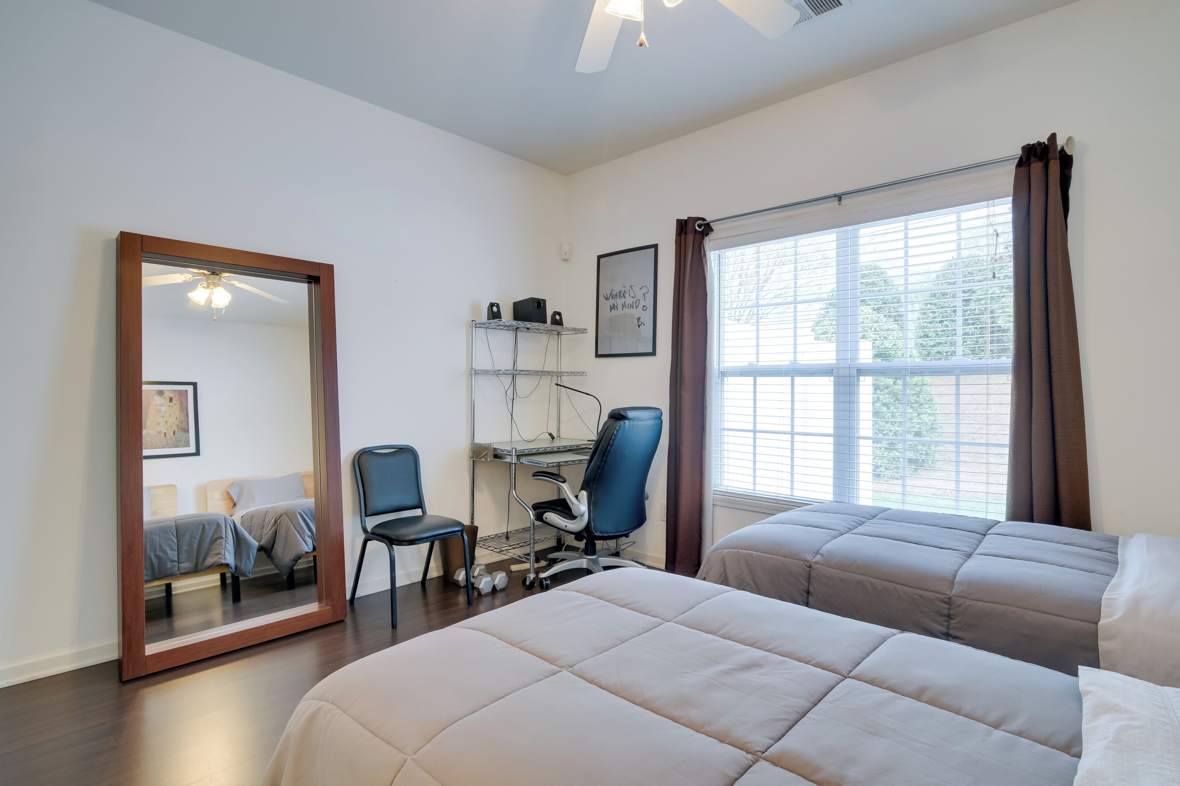 A hotel room with two beds, a desk, a chair, a ceiling fan, and a window with curtains.