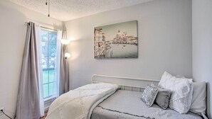 A bedroom with a bed, curtains, a window, and a cityscape painting on the wall. - Family-friendly Rowlett Home ~ 23 Mi to Dallas (Rowlett)