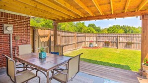 A covered patio with a wooden table and chairs, a brick wall, and a wooden fence in the background. - Family-friendly Rowlett Home ~ 23 Mi to Dallas (Rowlett)