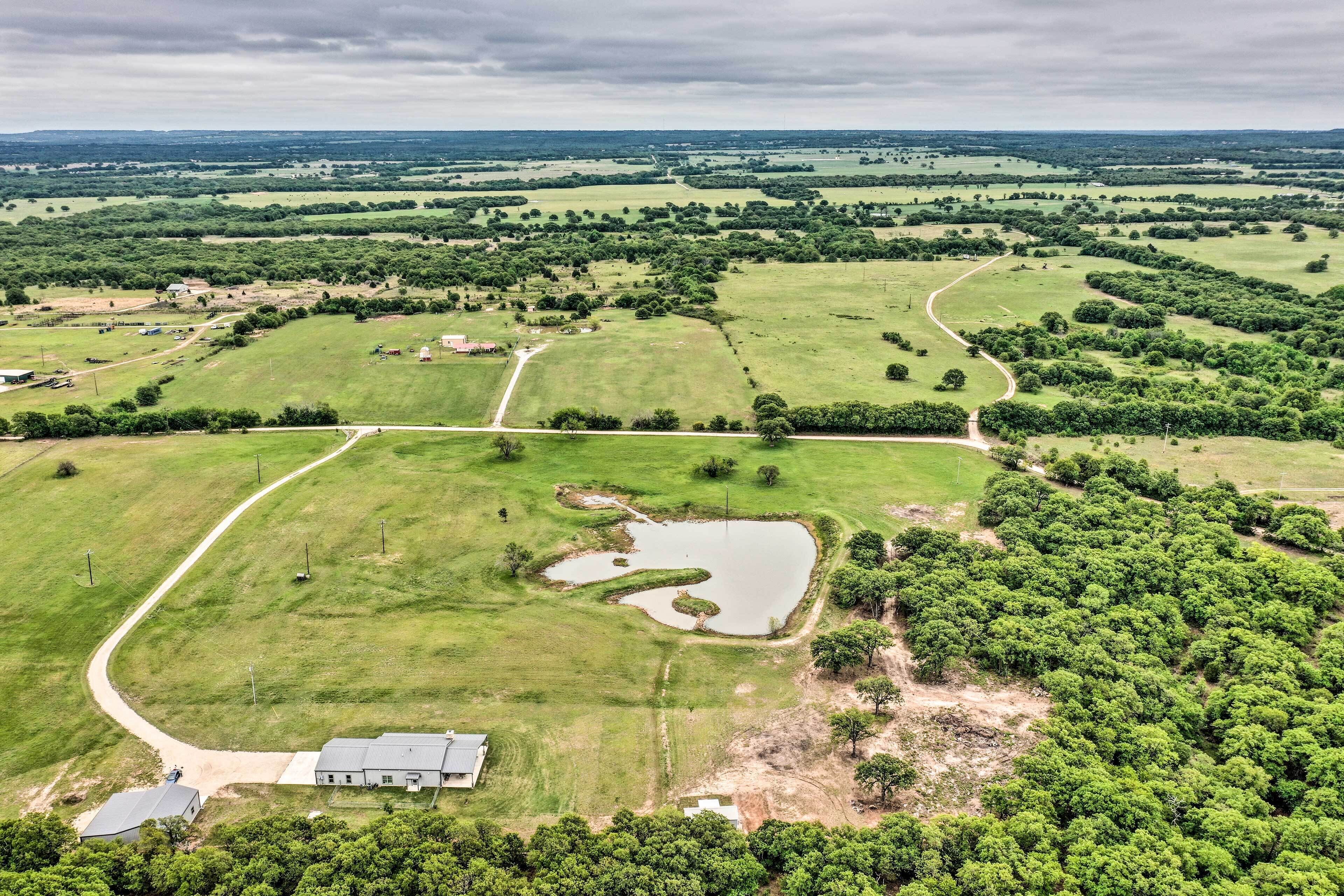 An aerial view of a rural landscape with a large green field, a small pond, and a few buildings.