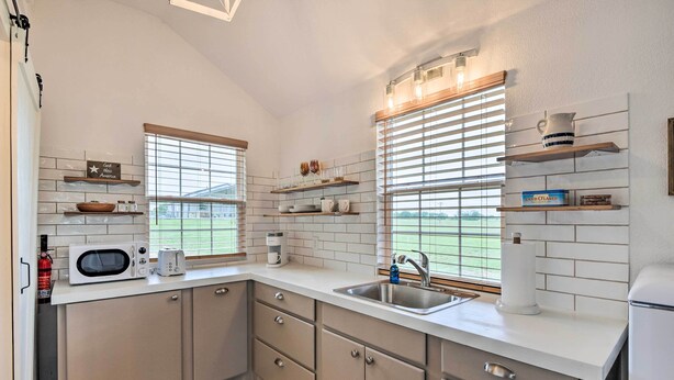 A modern kitchen with white cabinets, a microwave, toaster, and a sink. There are windows with blinds and a view of the outdoors. - On-site Pond & Fire Pit: Montague Retreat! (Montague)