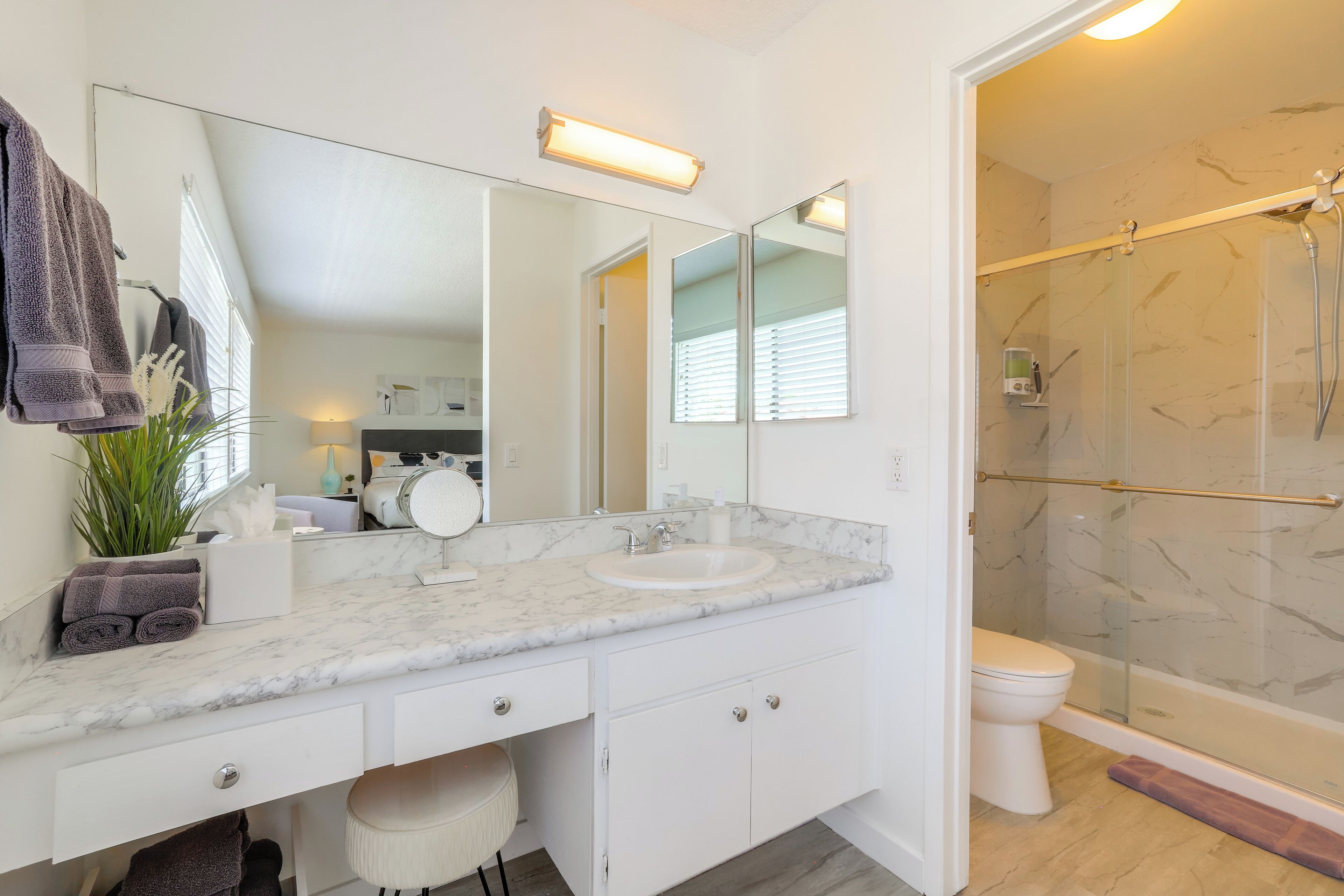 Et moderne badeværelse med marmorbordplade, et stort spejl, en glasbrusekabine og et hvidt toilet.
