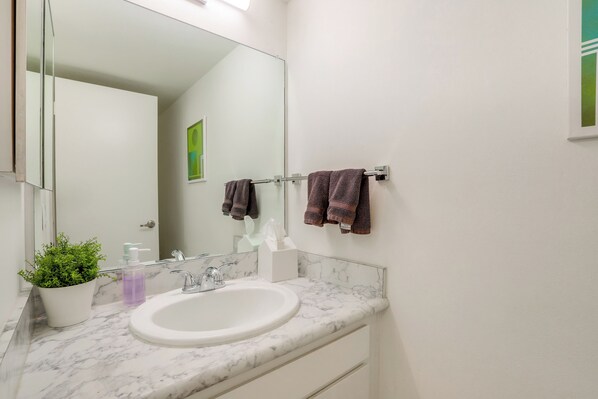 Un baño con un lavabo blanco, un espejo, un perchero con toallas, una planta en maceta y un dispensador de jabón.