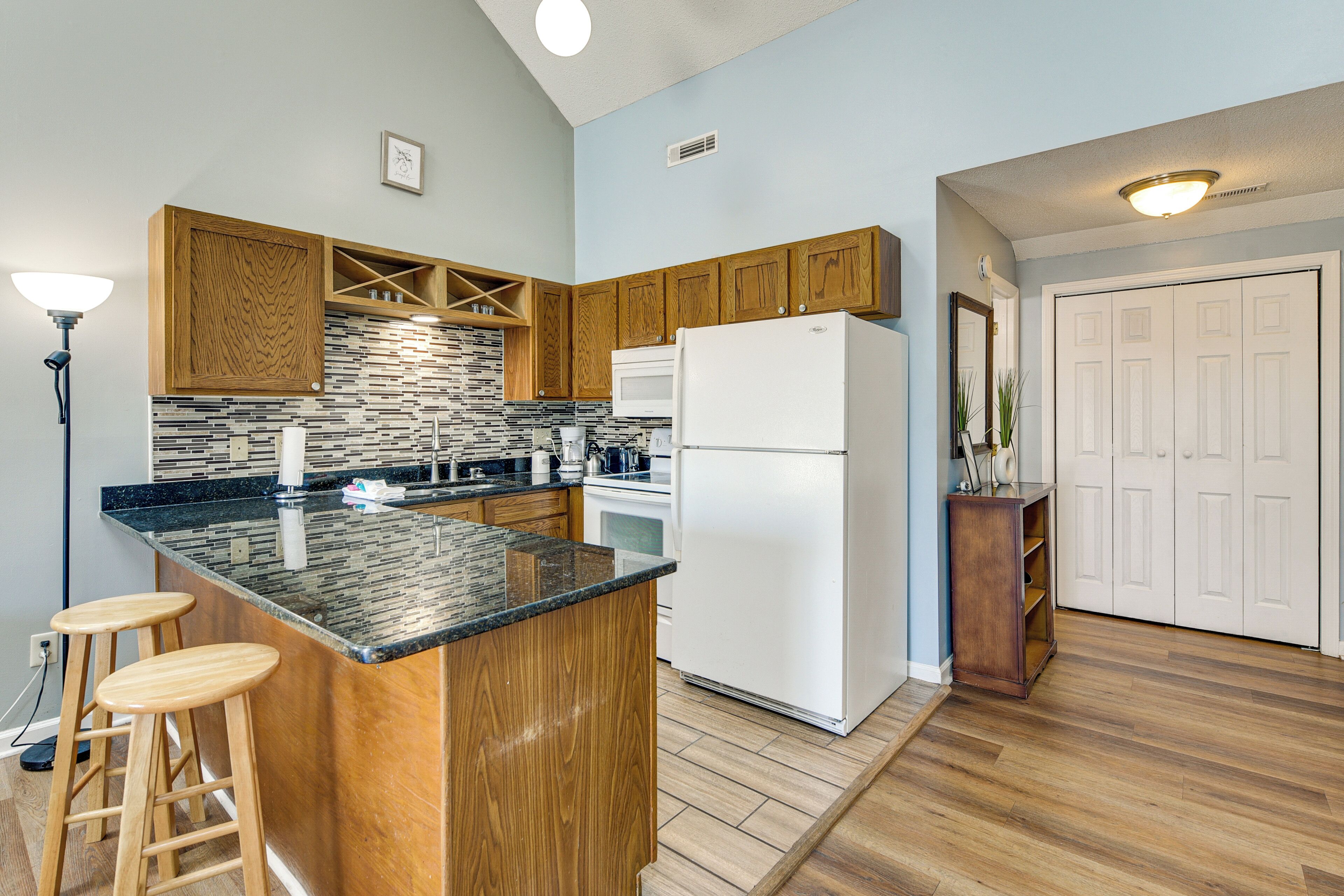 A kitchen with wooden cabinets, a black countertop, a white refrigerator, and a bar stool.