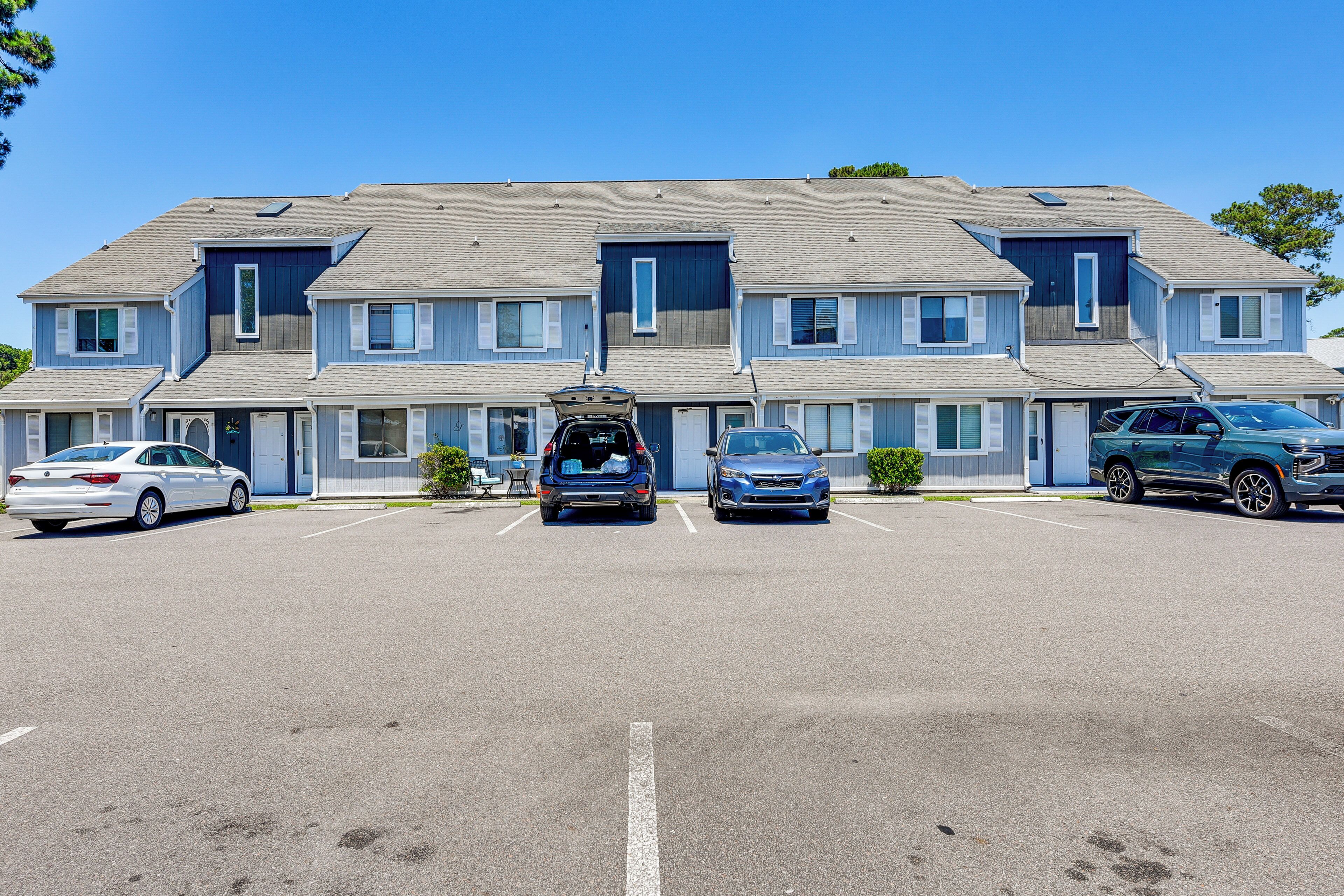 A multi-story hotel with a parking lot, a car in the driveway, and a blue car parked in the lot.