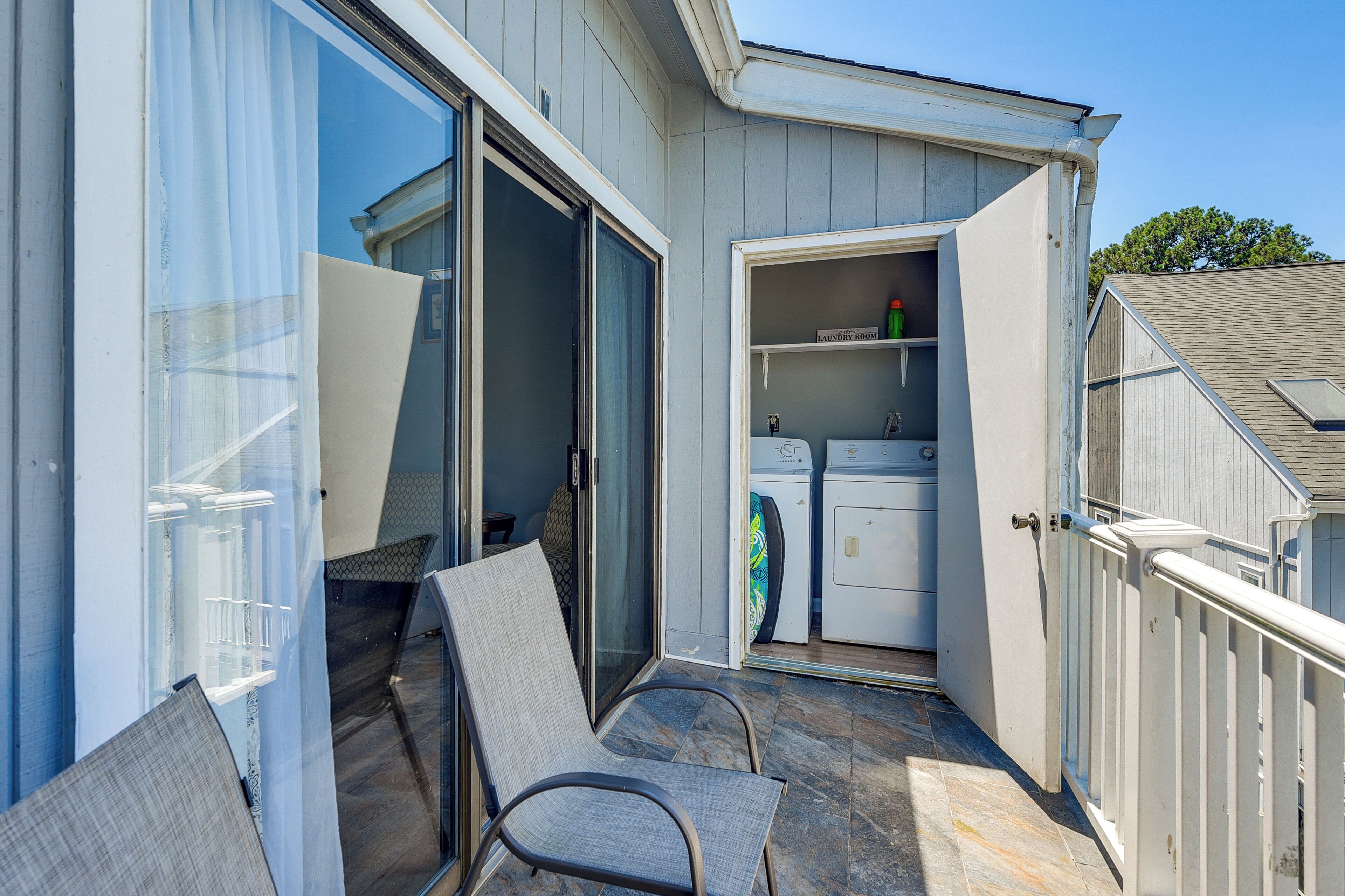 A residential property with a sliding glass door leading to a patio area with a chair, a laundry room with a washing machine and dryer, and a small storage cabinet.