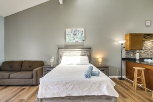 Un dormitorio con cama, mesita de noche, lámpara, sofá y una pequeña cocina.