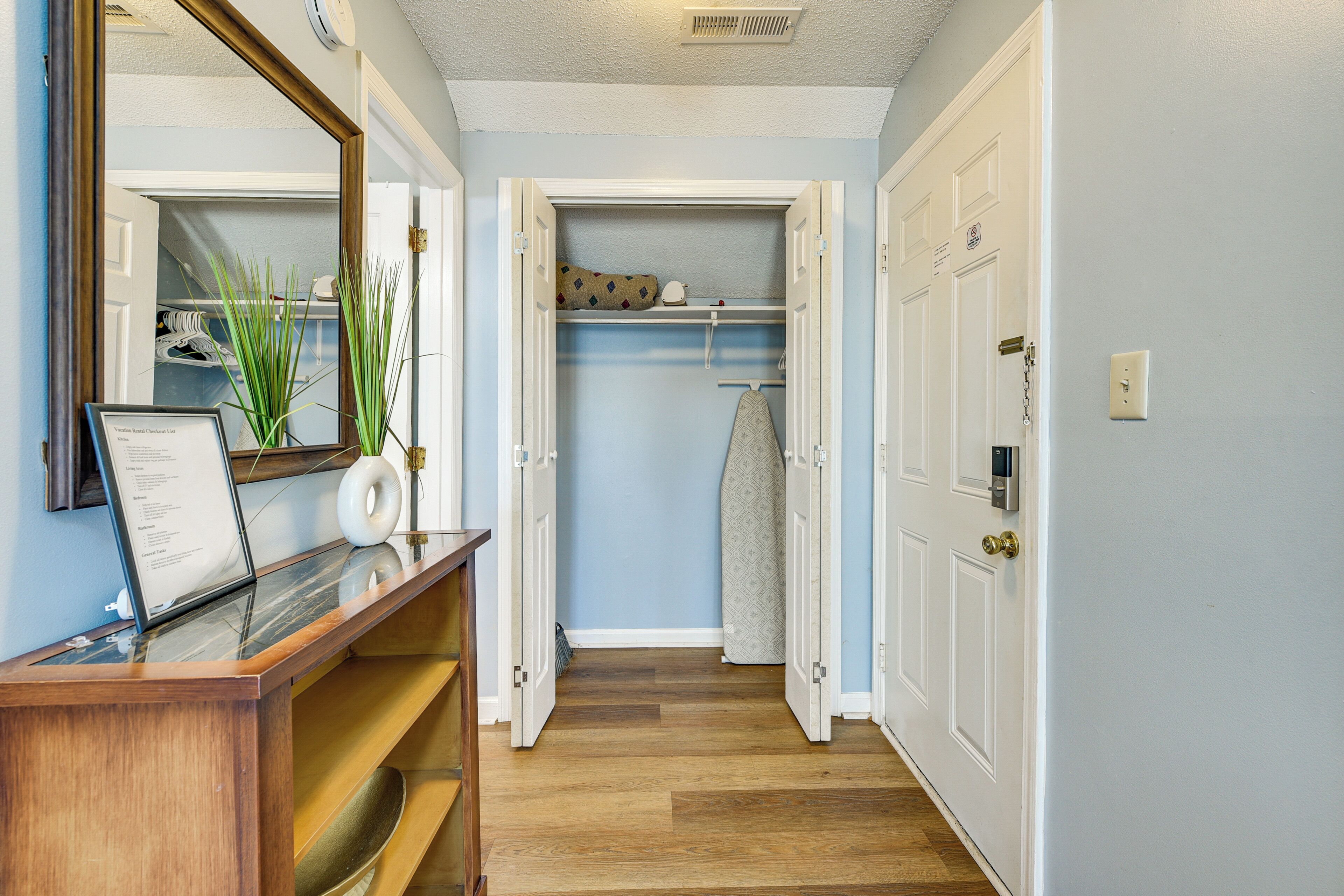 A hallway with a wooden reception desk, a mirror, and a closet with hanging clothes.