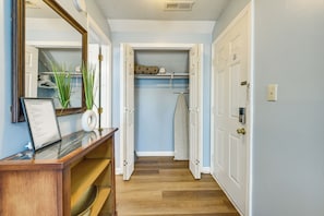 A hallway with a wooden reception desk, a mirror, and a closet with hanging clothes. - Cherry Grove Beach Studio w/ Heated Indoor Pool! (Little River)