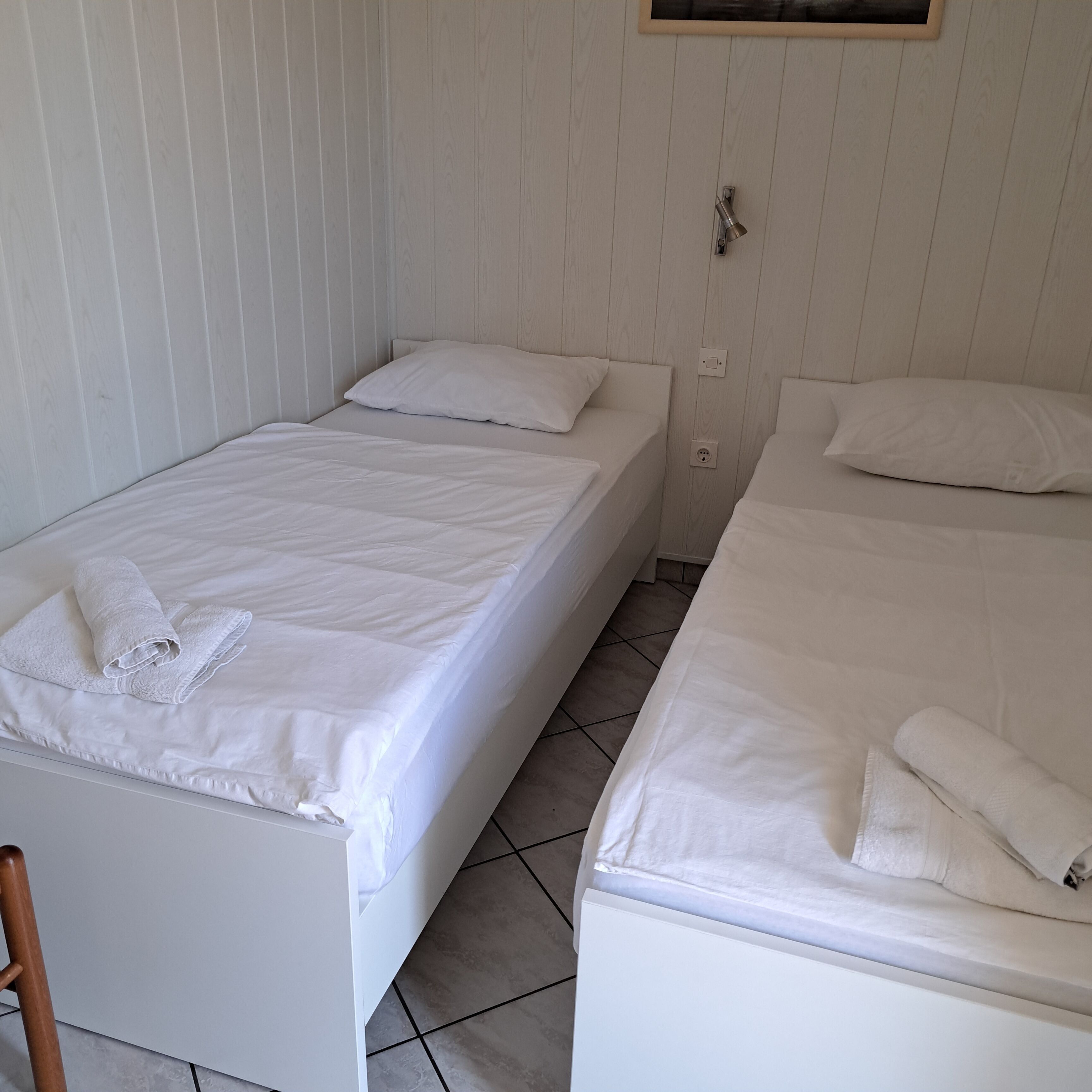 Een kamer met twee eenpersoonsbedden, elk met een kussen en een opgerolde handdoek.