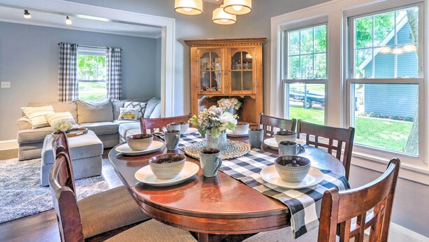 A dining area with a wooden table set for four, surrounded by chairs. A large wooden cabinet with glass doors is visible in the background.