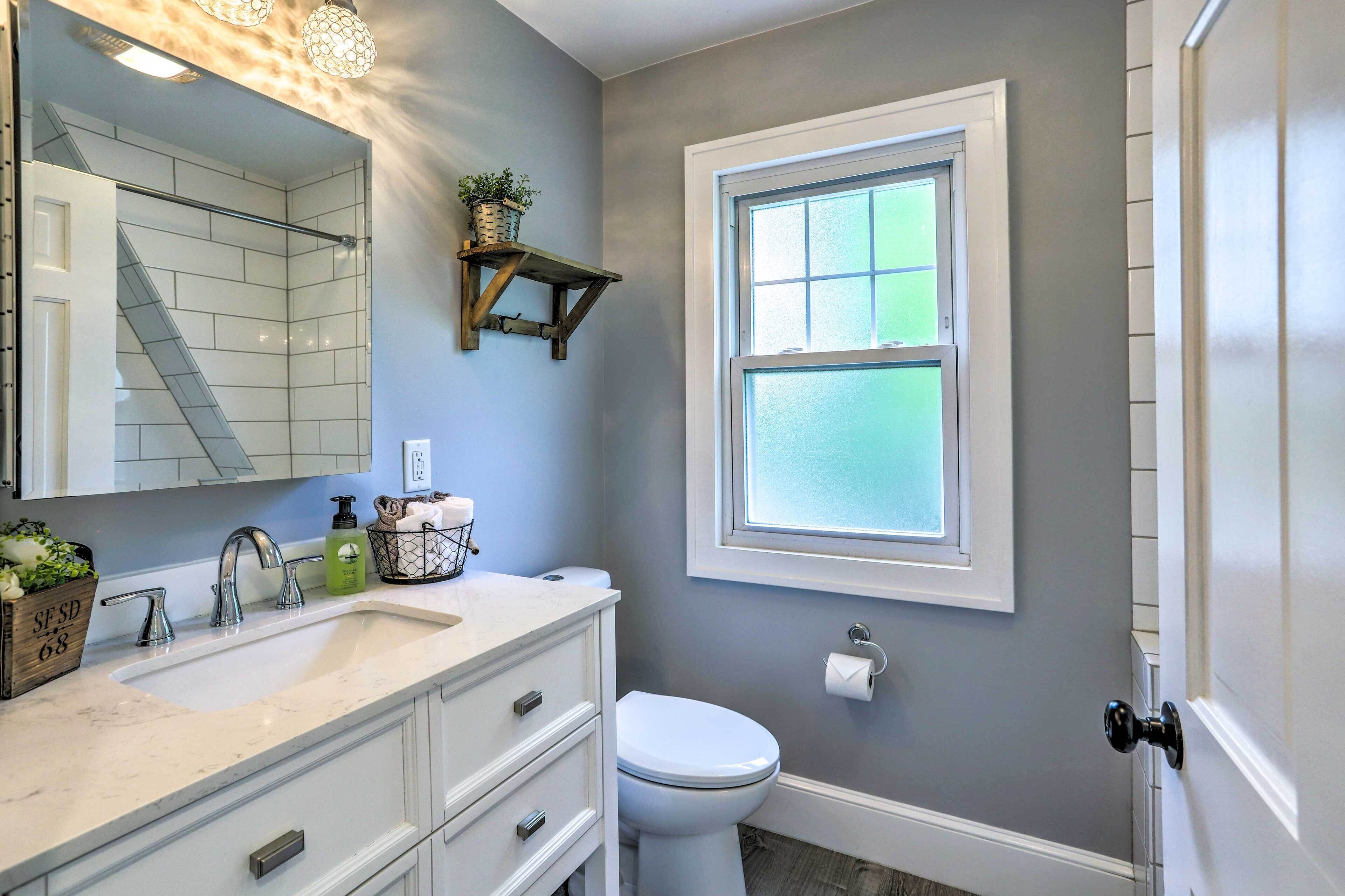 Une salle de bain avec un lavabo blanc, un miroir, des toilettes et une fenêtre.