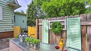 A patio with a glass table, a metal bucket with bottles, a potted plant, and two wine glasses.