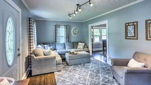 A living room with a grey sofa, ottoman, and a patterned rug. There is a clock on the wall and a chandelier.