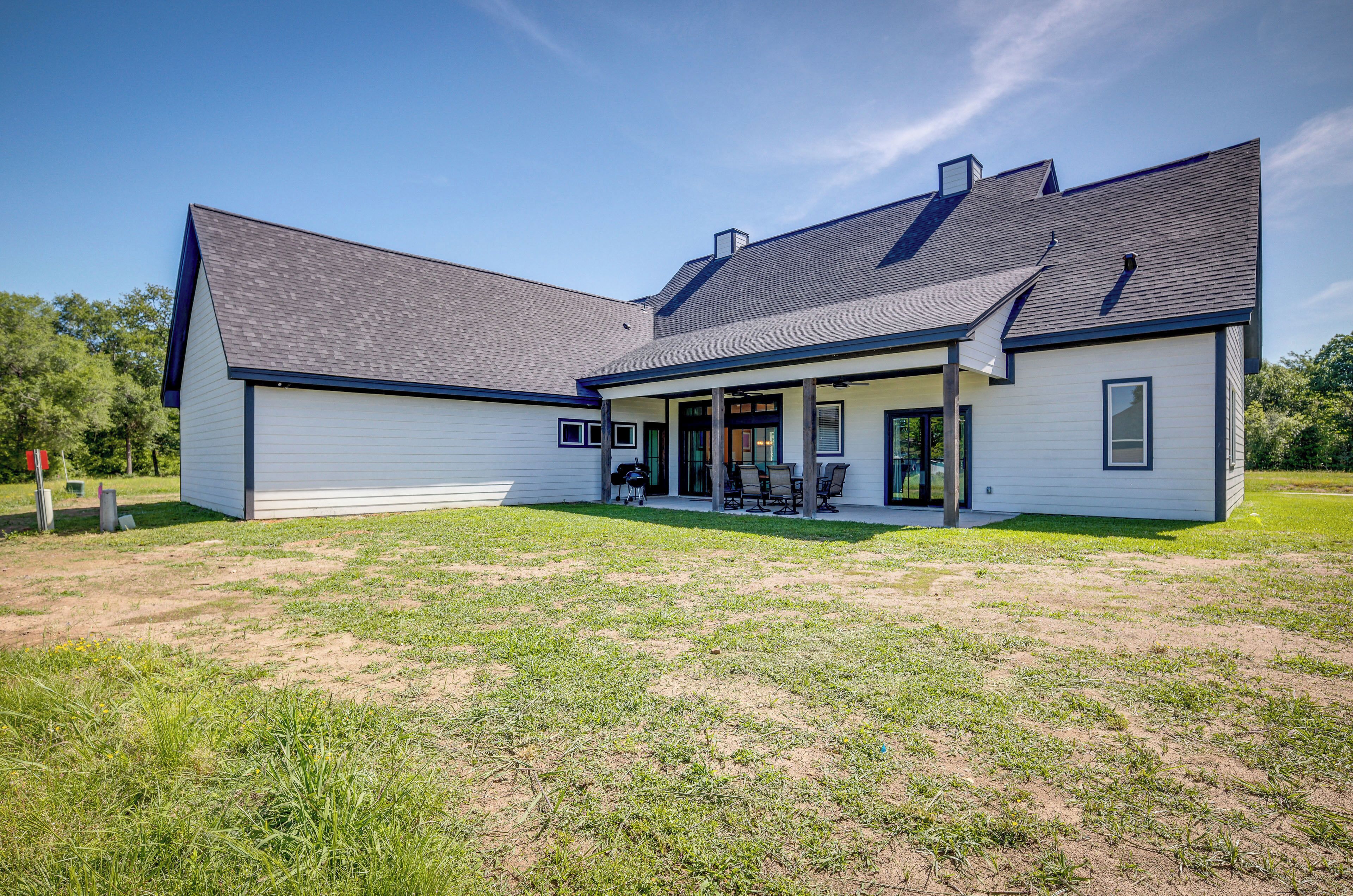 A two-story house with a covered patio area, a large lawn, and a clear sky.