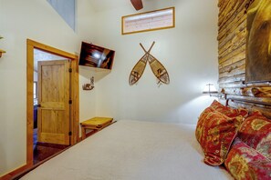 Ein Schlafzimmer mit einem Bett, einer Holztür, einem an der Wand befestigten Fernseher und Wanddekorationen.