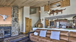 A spacious living area with a stone fireplace, a leather sofa, and a kitchen in the background. - Ski, Soak & Explore! Granby Getaway w/ Mtn Views (Granby)