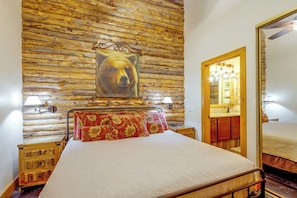 A bedroom with a wooden log wall, a bed with red patterned pillows, a wooden nightstand, a mirror, and a ceiling fan. - Ski, Soak & Explore! Granby Getaway w/ Mtn Views (Granby)