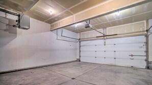 Eine Garage mit geschlossener weißer Rolltür, Betonboden und sichtbarer Elektroinstallation.