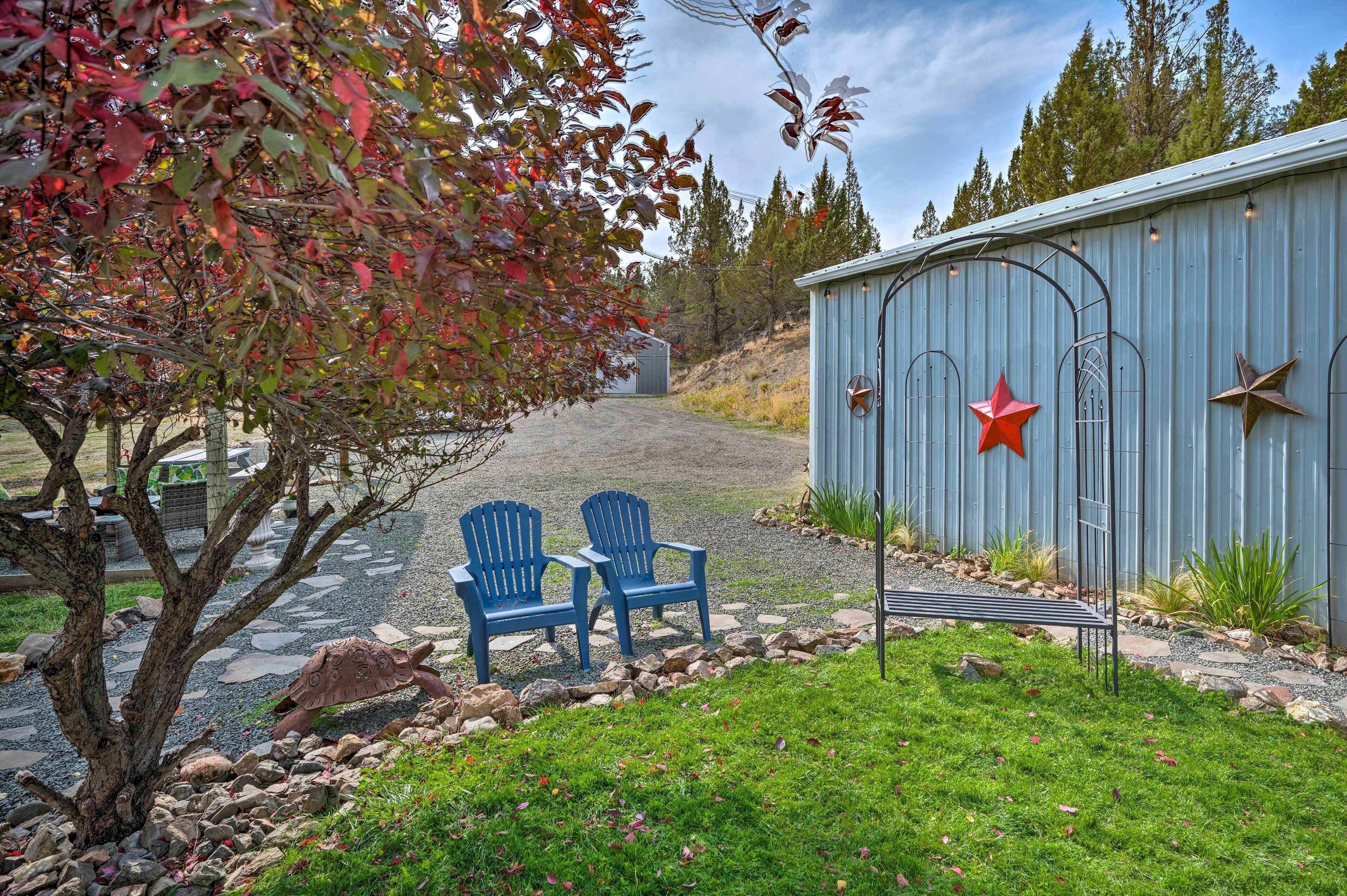 A rustic outdoor seating area with two Adirondack chairs, a metal bench, and a shed with decorative stars.