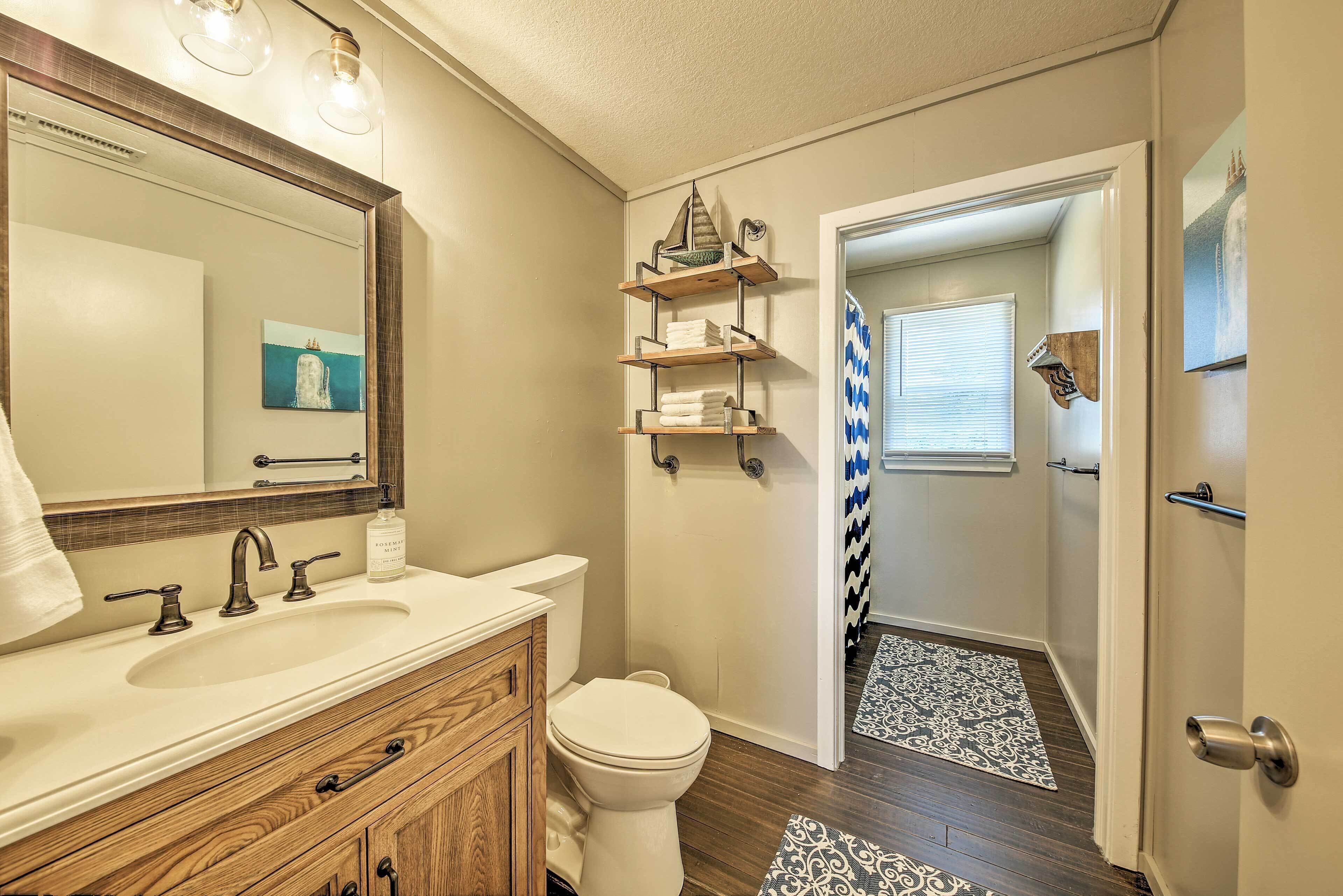 Une salle de bain avec un meuble-lavabo, un évier et des toilettes. Il y a des étagères au-dessus des toilettes et un miroir avec des lumières.