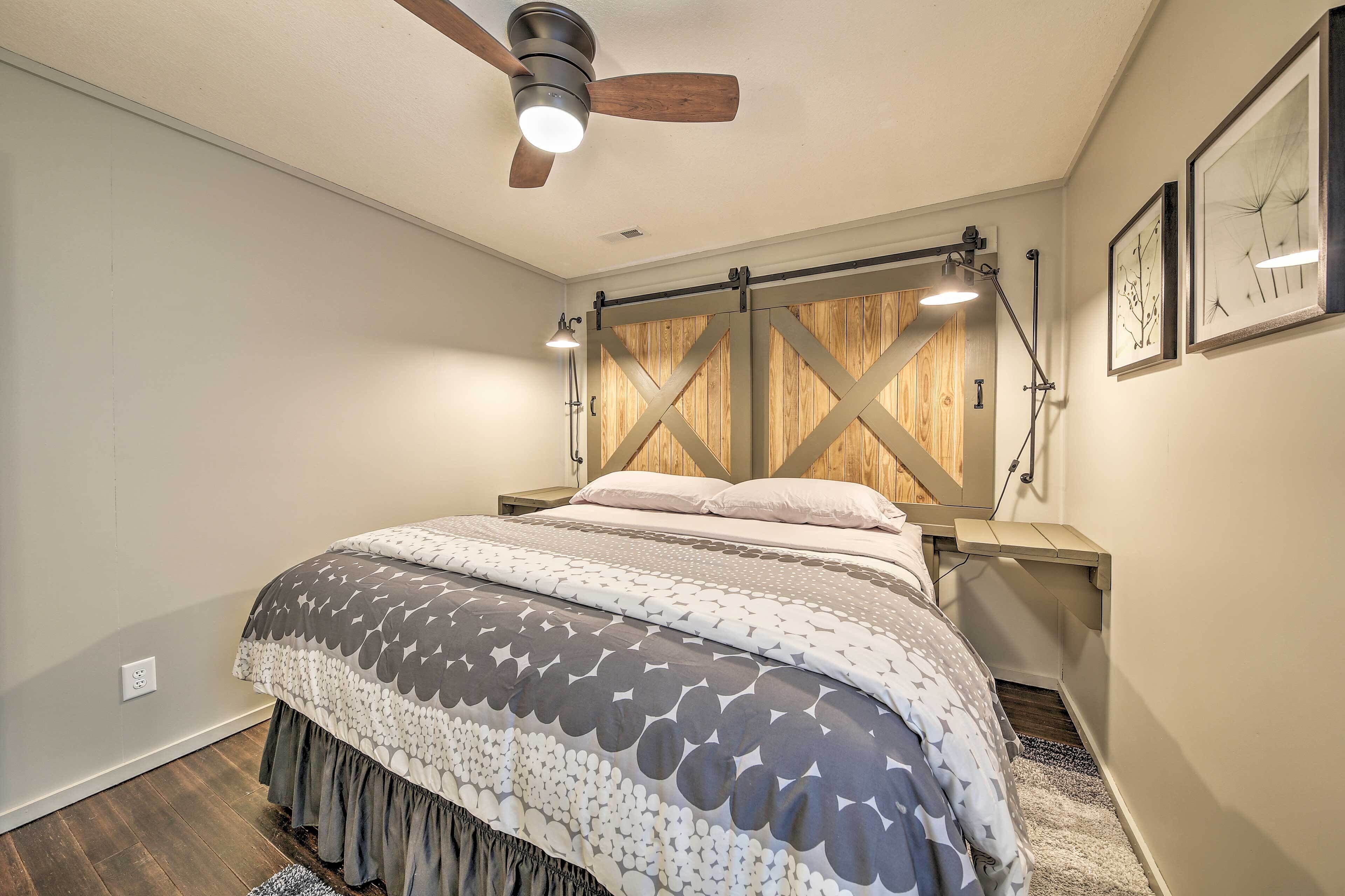 Una camera da letto con un letto, una testiera in legno, una ventola a soffitto, lampade sui comodini e un quadro appeso al muro.