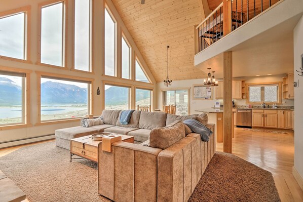 Ein geräumiges Wohnzimmer mit einem großen Ecksofa, Holzboden und großen Fenstern mit Blick auf die Berge.
