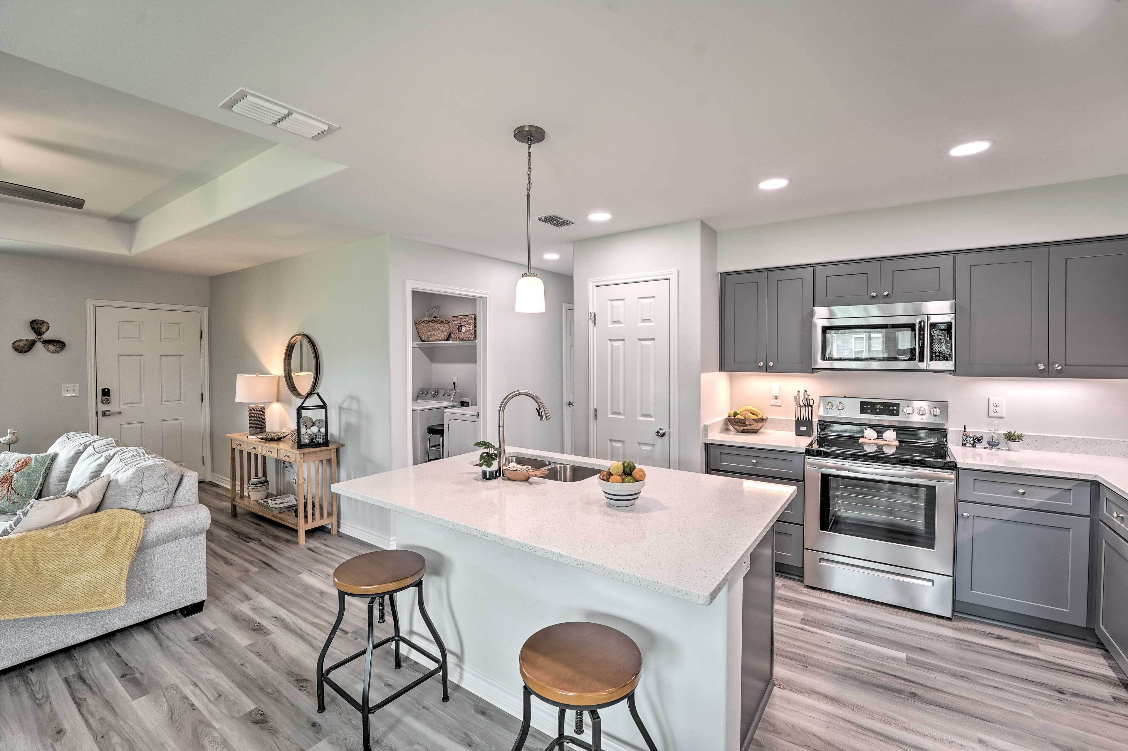 A modern kitchen with grey cabinets, a stainless steel oven, and a central island with stools.