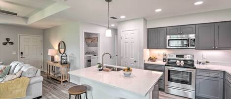 A modern kitchen with grey cabinets, a stainless steel oven, and a central island with stools.