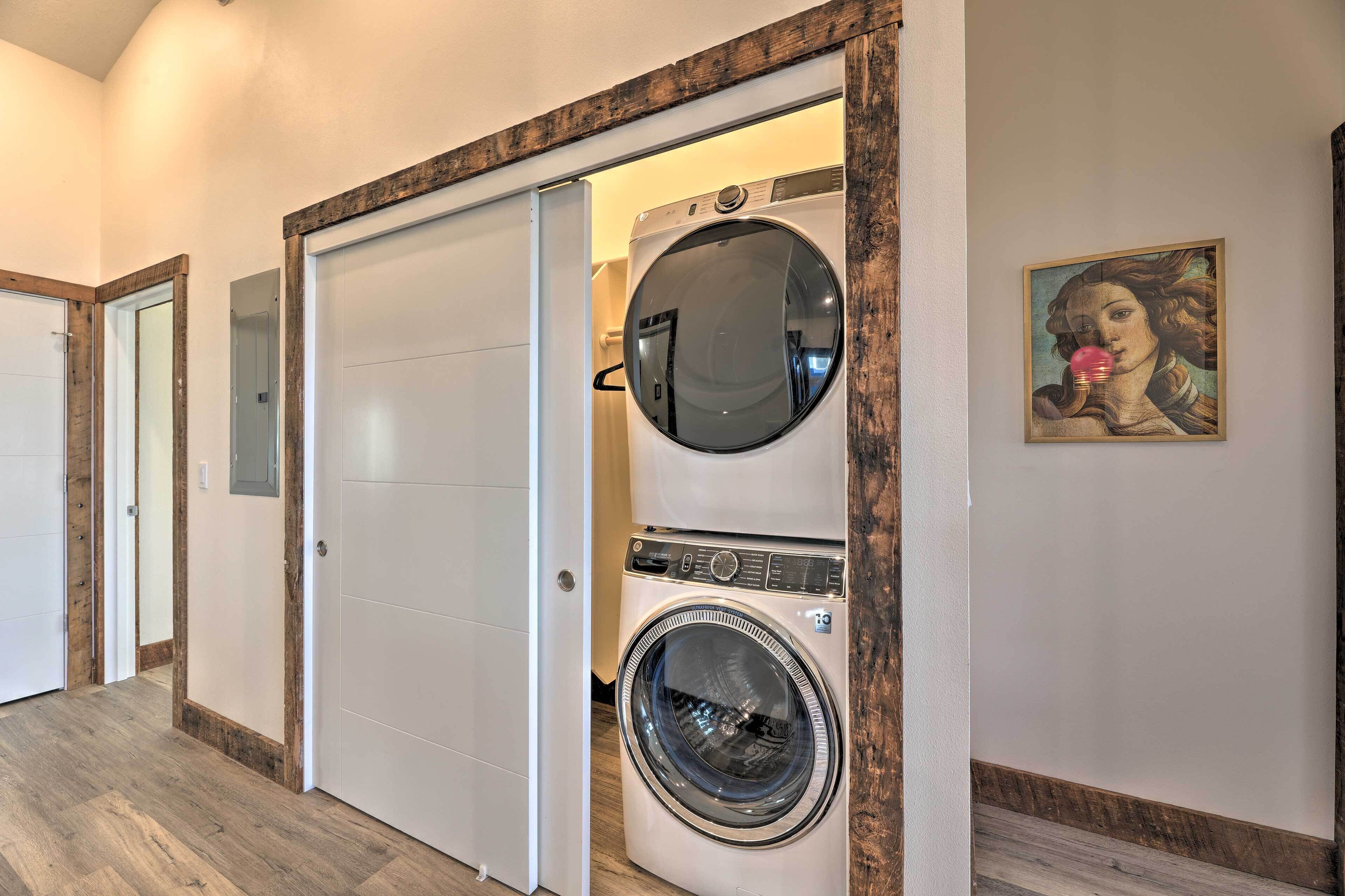 A laundry room with a front-loading washer and dryer, wooden trim, and a painting on the wall.