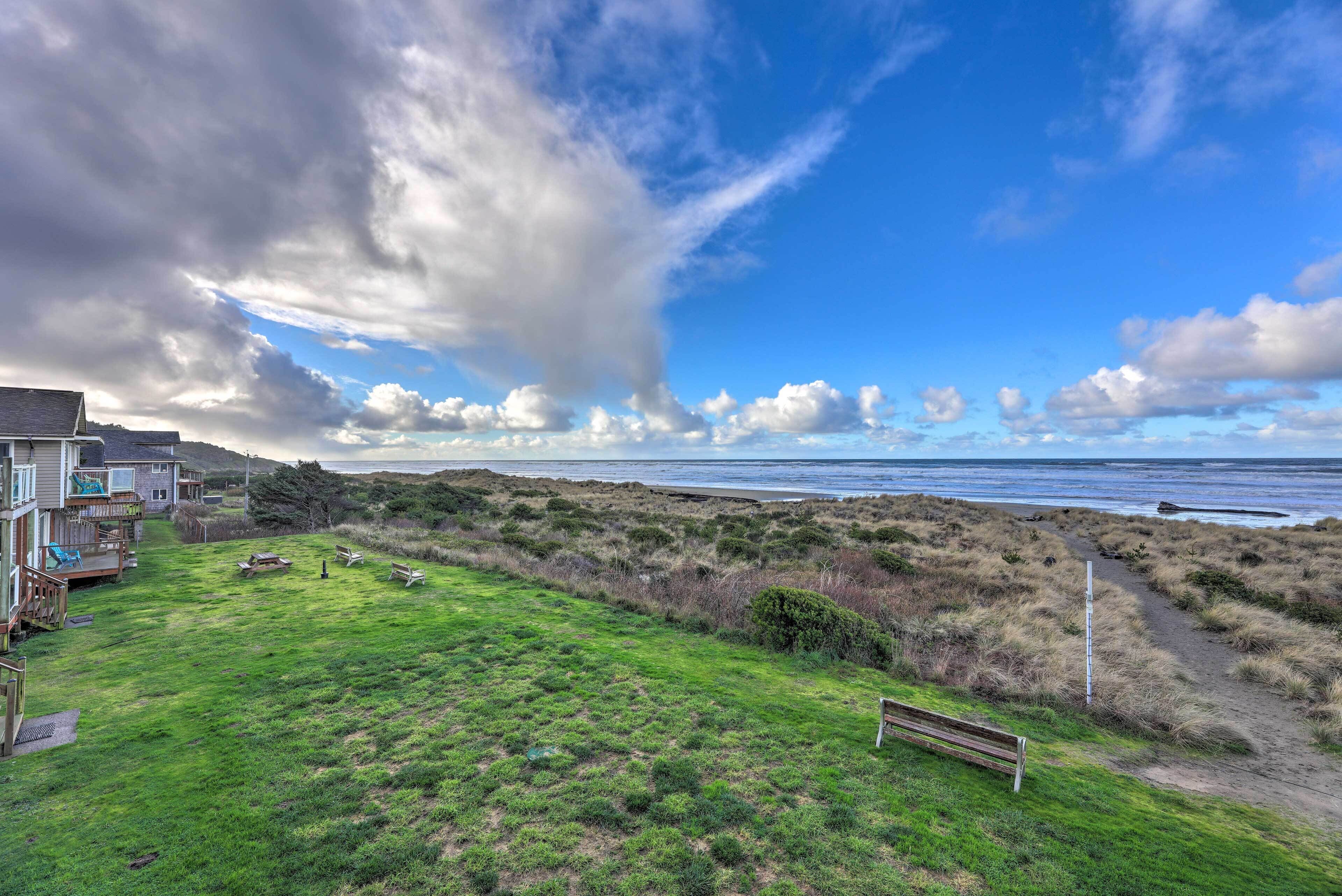 A coastal property with a grassy lawn, a wooden deck, and a bench overlooking the beach.