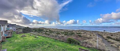 A coastal property with a grassy lawn, a wooden deck, and a bench overlooking the beach.