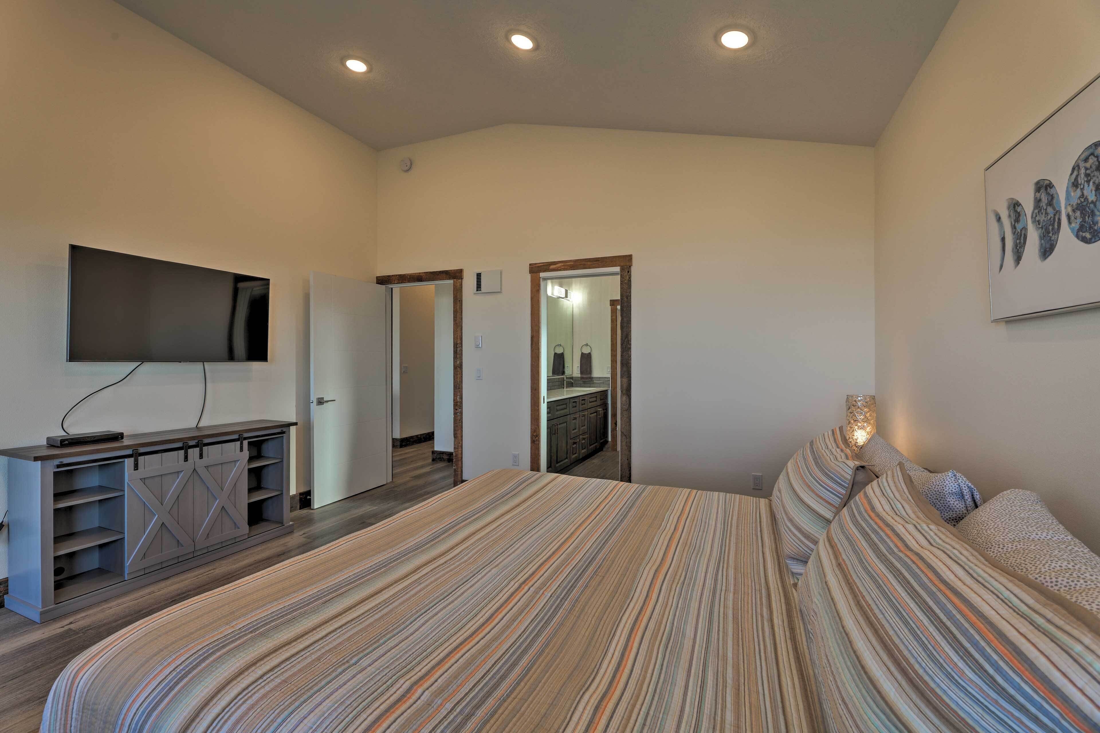 Een slaapkamer met een groot bed, een televisie op een kast, een deur naar een badkamer, en een kunstwerk aan de muur.