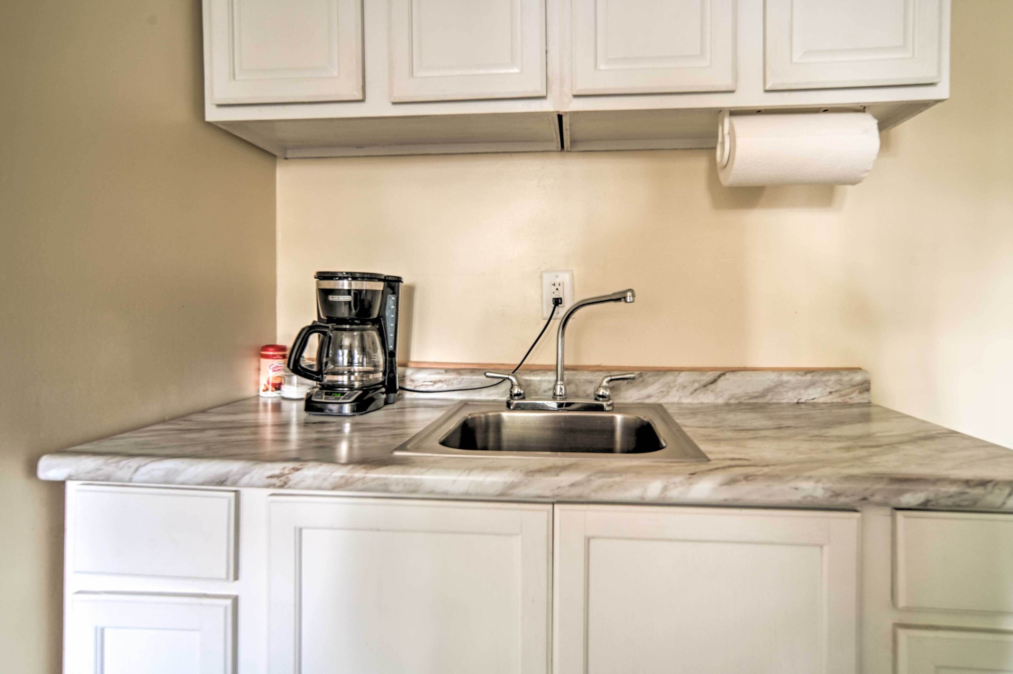 A kitchen with white cabinets, a stainless steel sink, a coffee maker, and a roll of paper towels.