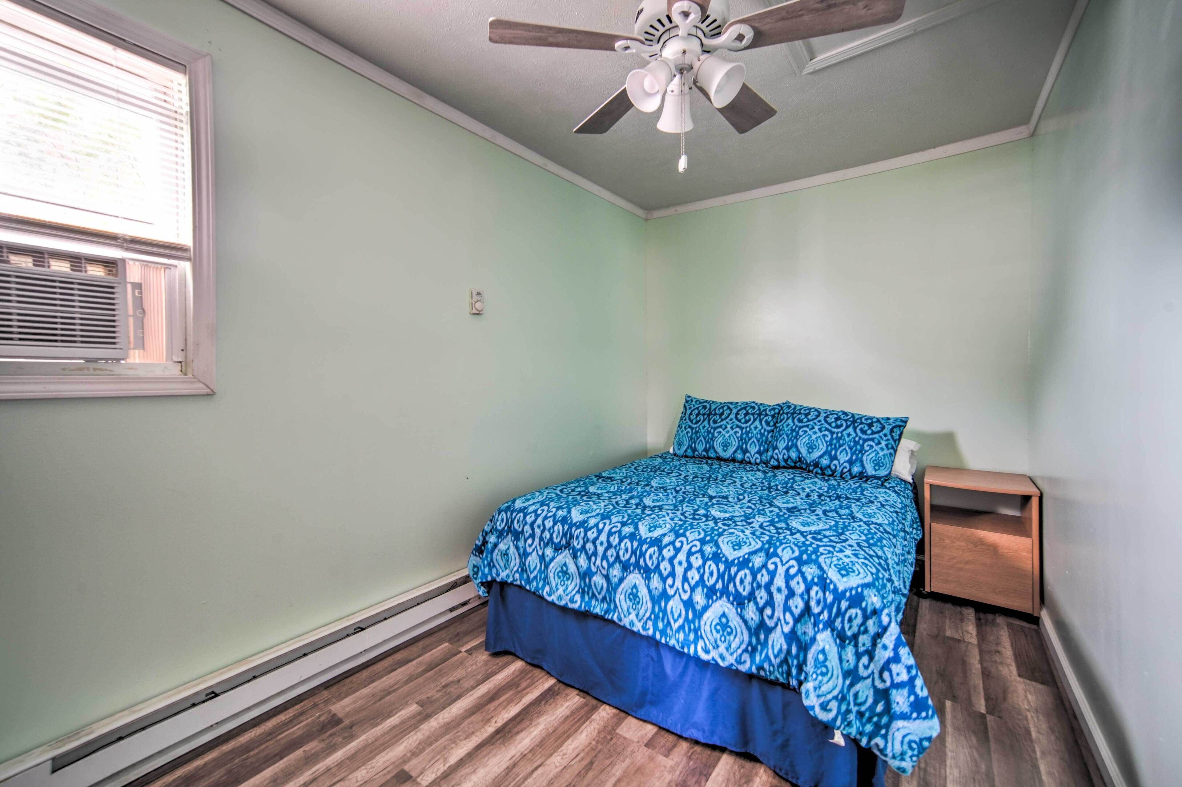 A bedroom with a bed, a nightstand, a ceiling fan, and a window.