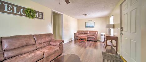 A living room with a brown leather sofa, a wooden coffee table, a ceiling fan, and a welcome sign on the wall.