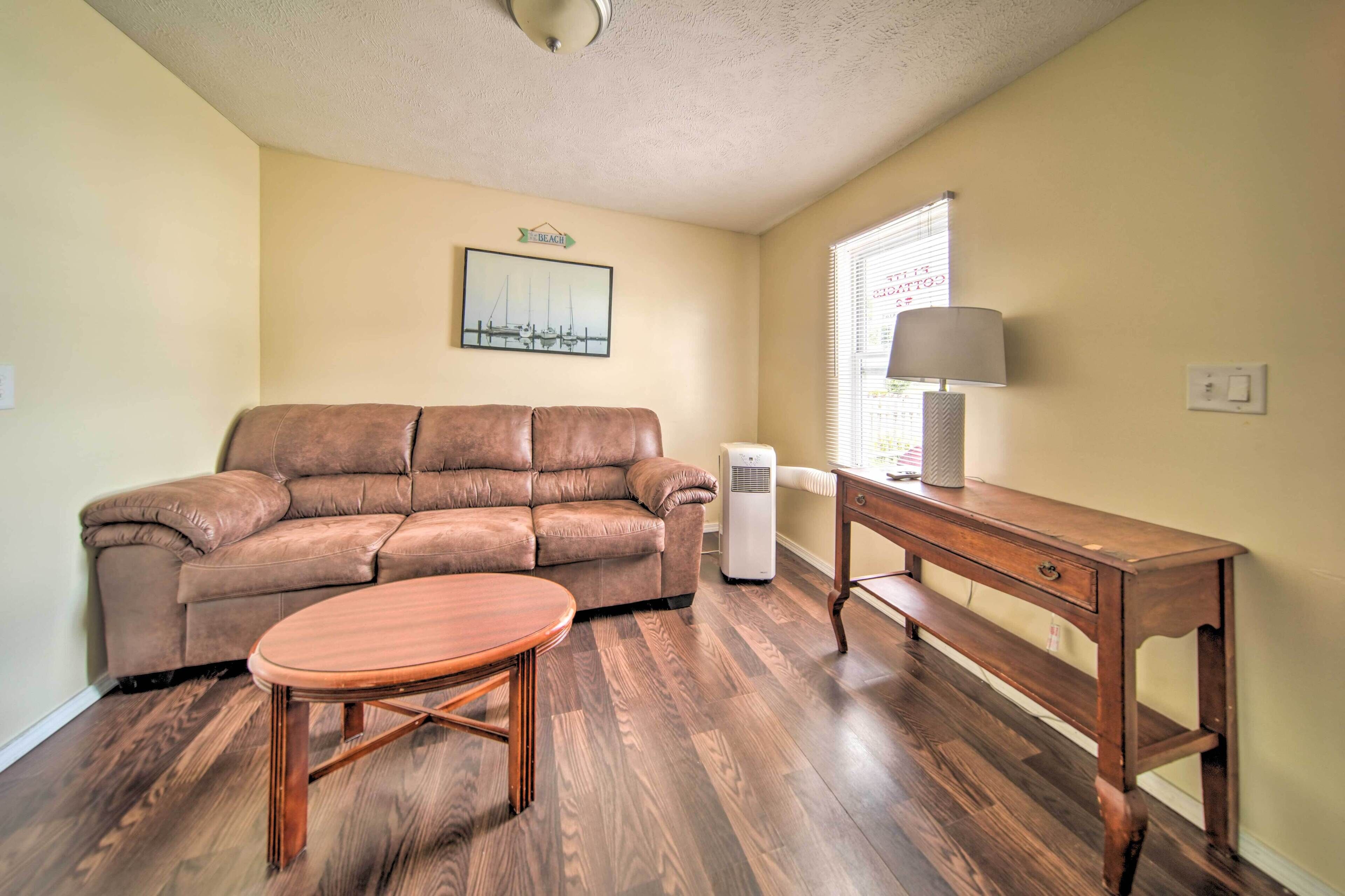A living room with a brown leather sofa, a wooden coffee table, a wooden side table with a lamp, and a white air conditioner.