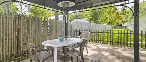 An outdoor patio with a round table and chairs, a metal lamp, and a wooden fence.