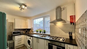A modern kitchen with white cabinets, a built-in washing machine, a gas stove, and a window with potted plants. - Daubney House (Cleethorpes)