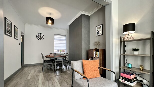 A modern living room with a grey sofa, a dining table with chairs, a bookshelf, and a clock on the wall. - Daubney House (Cleethorpes)