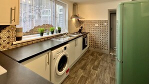 A compact kitchen with a built-in washer, a window with lace curtains, and a green refrigerator. - Daubney House (Cleethorpes)