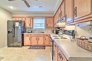 A kitchen with wooden cabinets, a stainless steel refrigerator, a stove, and a window with blinds. - Park Once, Walk to Every Ole Miss Tradition (Oxford)