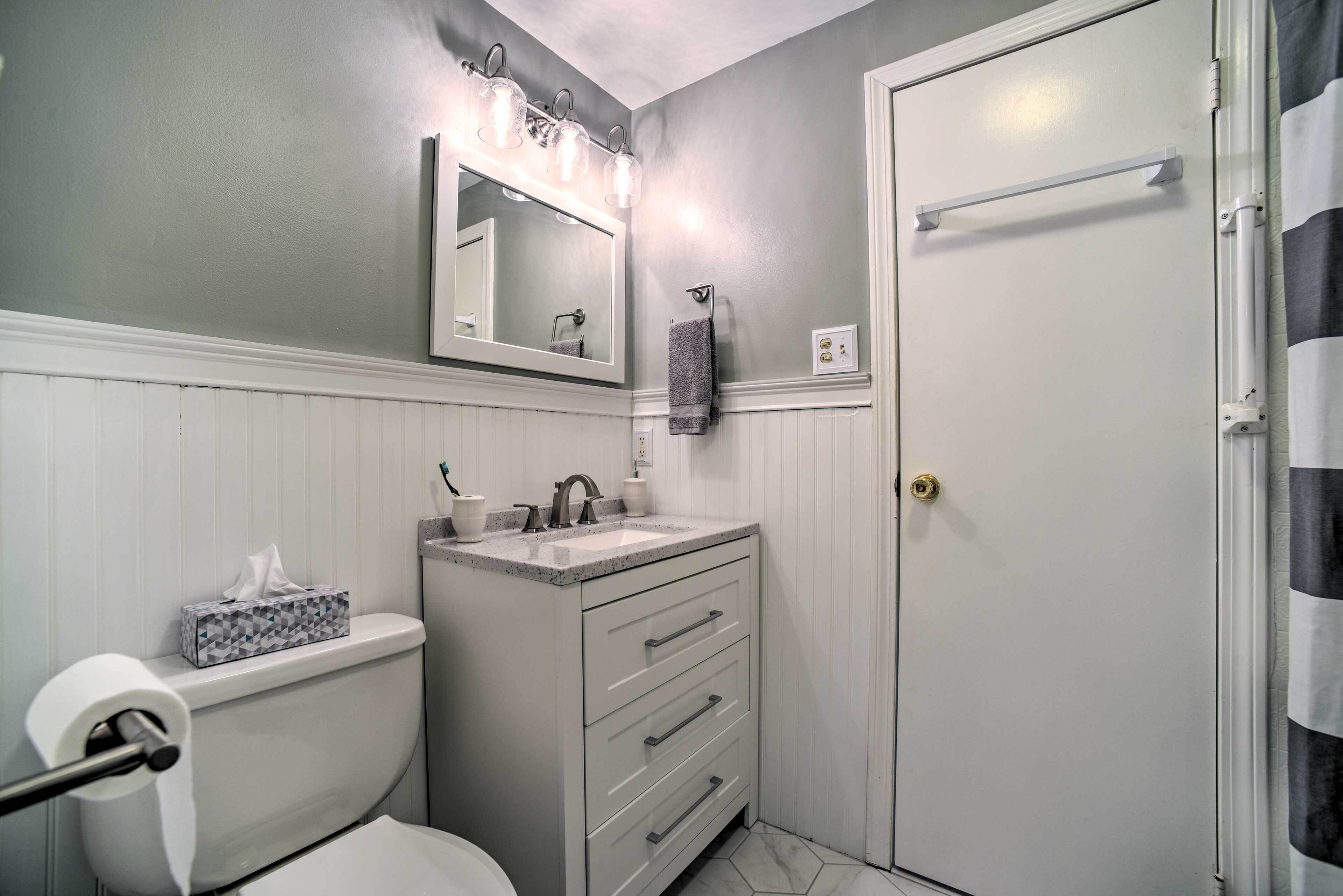A bathroom with a toilet, sink, vanity, and a mirror with lights.