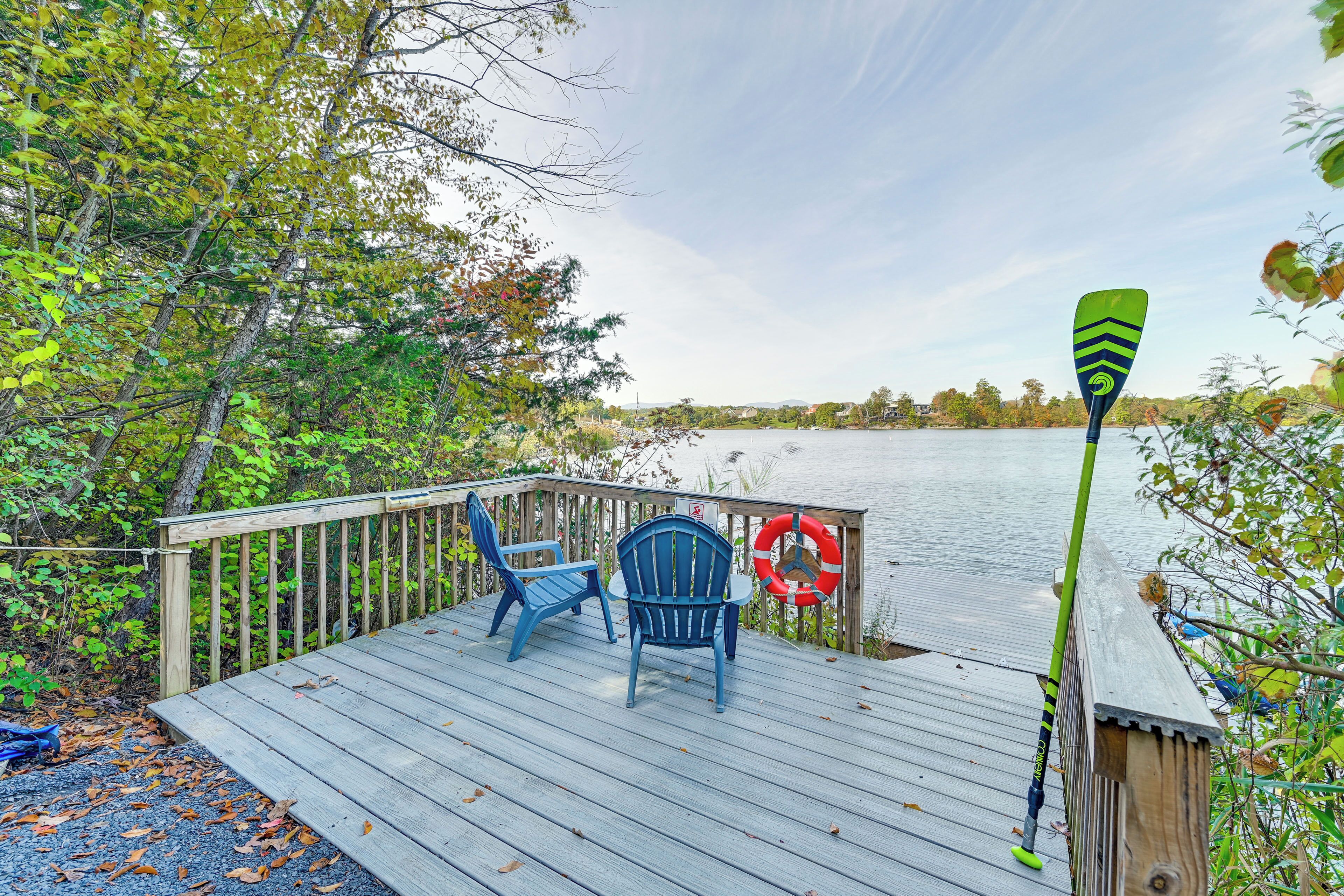 A wooden deck with two blue Adirondack chairs and a green paddle.
