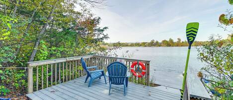 A wooden deck with two blue Adirondack chairs and a green paddle.