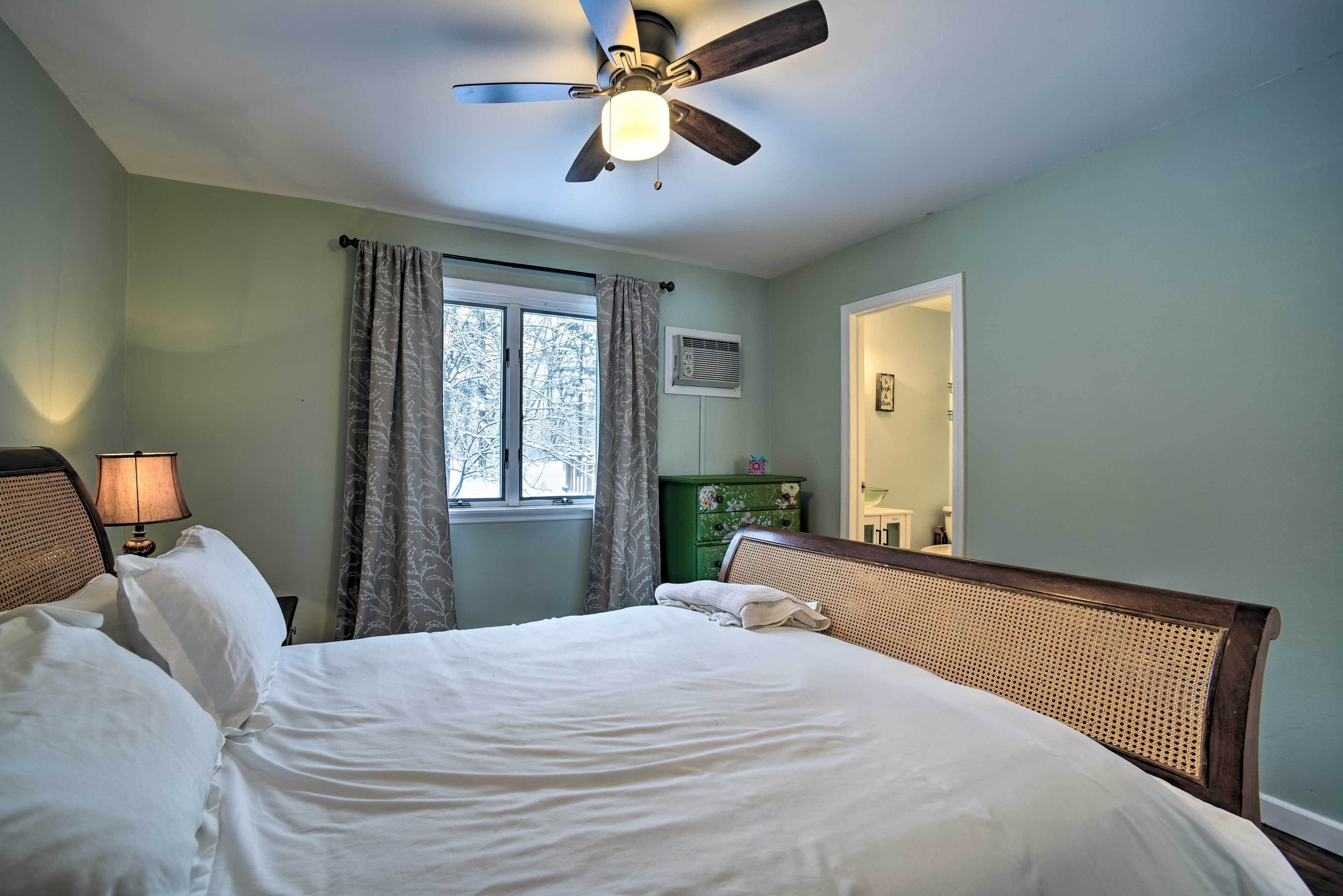 Un dormitorio con cama, ventilador de techo, ventana con cortinas, cómoda y espejo.