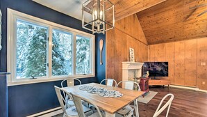 Een eethoek met een houten tafel, witte stoelen en een groot raam met uitzicht op met sneeuw bedekte bomen.