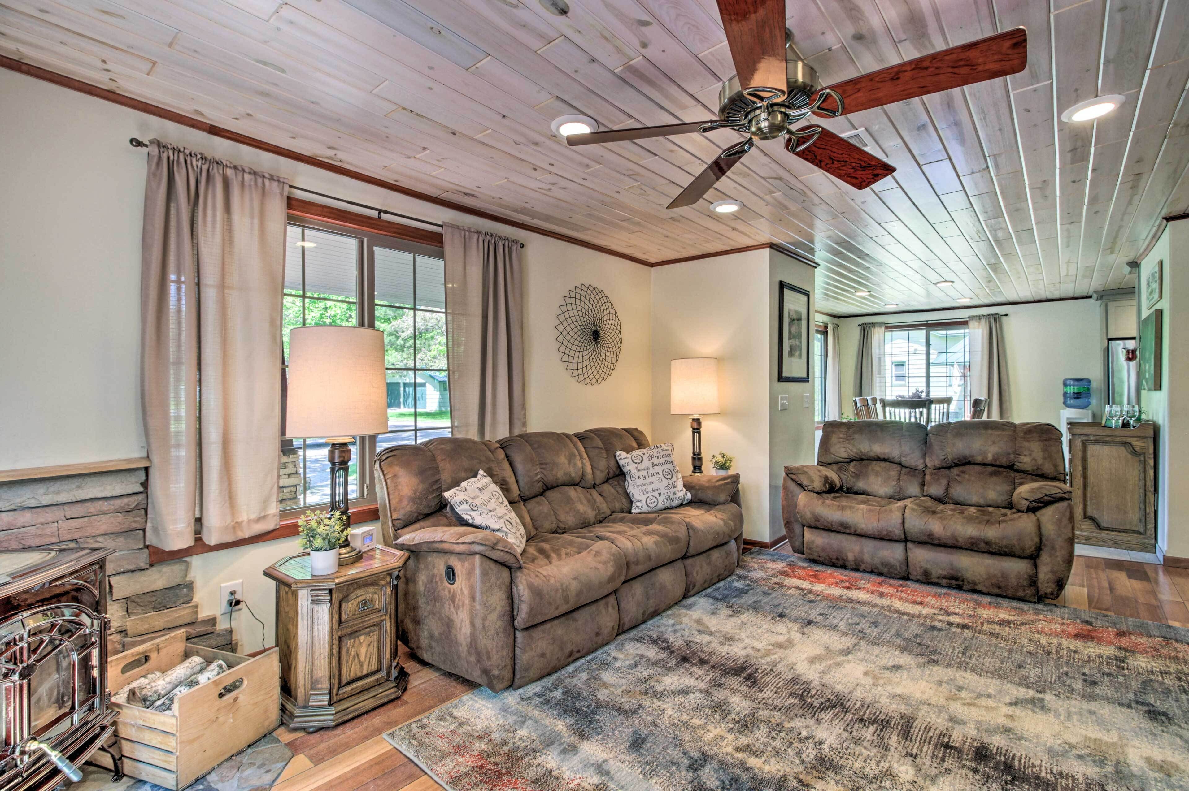 A cozy living room with two brown sofas, a wooden ceiling fan, and a large rug.