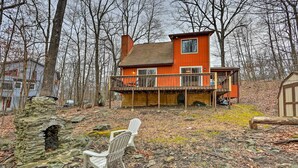 A two-story house with a balcony, surrounded by trees and a stone structure. - 4 Mi to Tubing: Cozy Bushkill Cabin w/ Deck! (Bushkill)